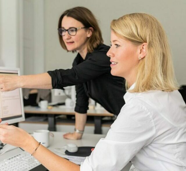 Zwei Frauen schauen auf einen Computerbildschirm.