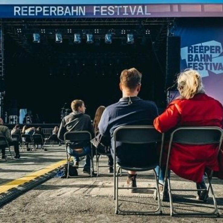 Menschen sitzen bei dem Reeperbahnfestival vor einer Bühne.